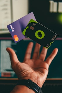 a hand holding a credit card in front of a computer
