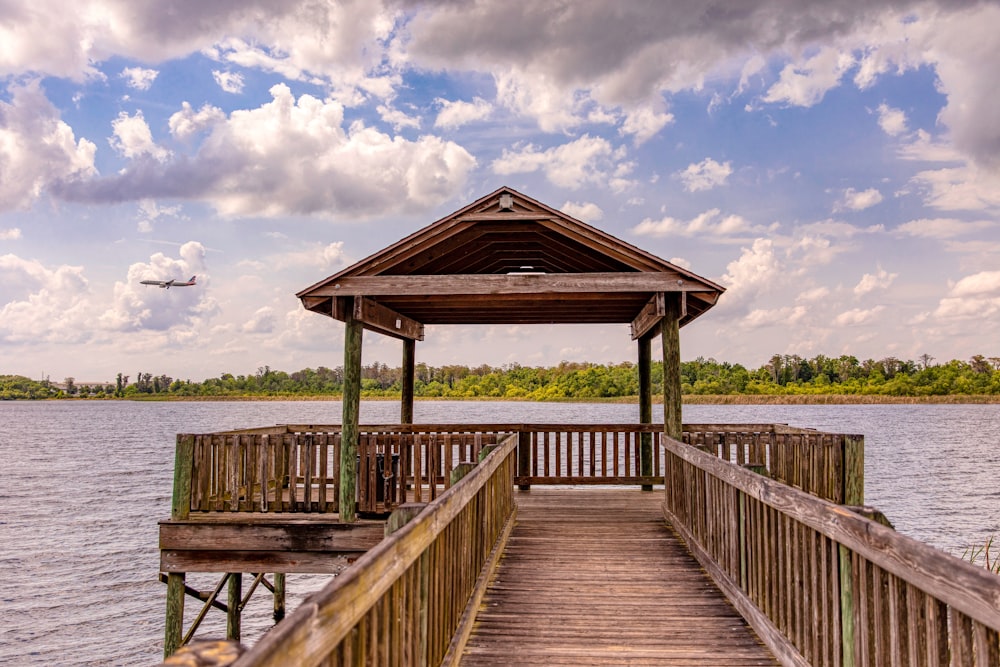 a dock with a gazebo and a plane in the sky