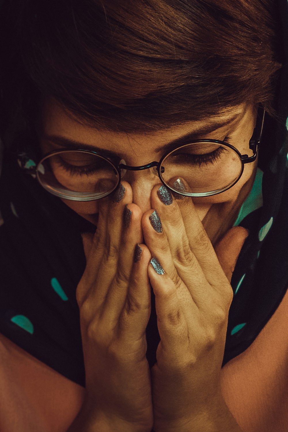 a woman wearing glasses covers her face with her hands