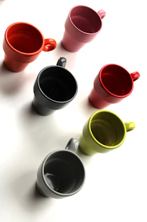 Set of colorful ceramic mugs with unique shapes and glossy finishes arranged on a shelf