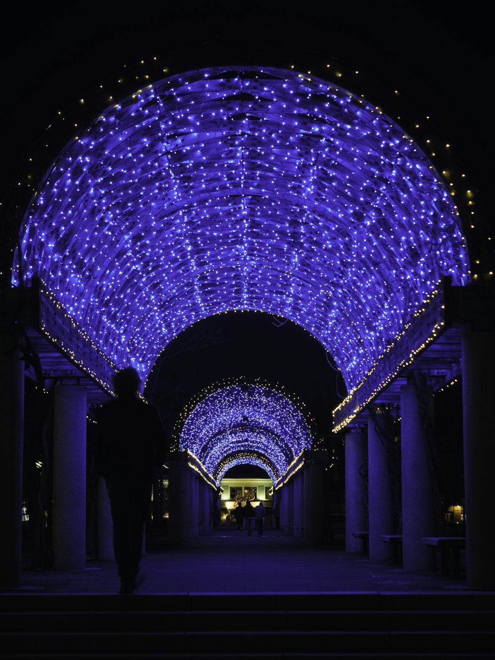 a man walking down a walkway covered in blue lights