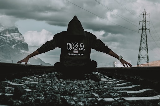 a person sitting on a train track with their arms outstretched