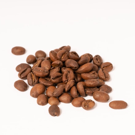 A pile of roasted coffee beans scattered on a white surface.