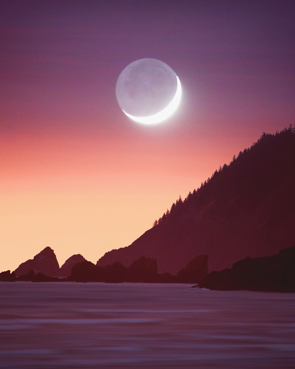 a crescent moon is seen over the ocean