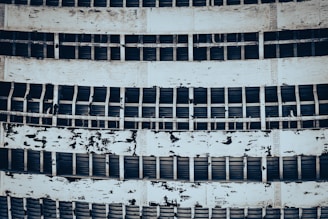 A detailed view of an industrial structure featuring several horizontal metal beams and flaking paint on sheets. The repeated pattern of beams and peeling layers gives an aged and weathered appearance.