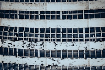 A detailed view of an industrial structure featuring several horizontal metal beams and flaking paint on sheets. The repeated pattern of beams and peeling layers gives an aged and weathered appearance.