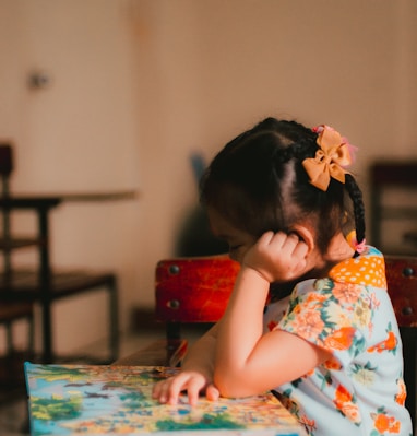a little girl sitting at a table with a book