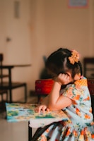 a little girl sitting at a table with a book