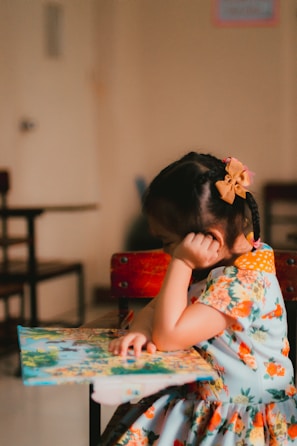 a little girl sitting at a table with a book