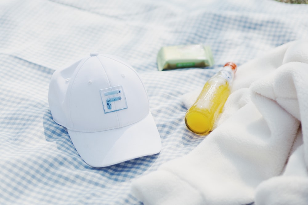 a cap, a bottle of liquid and a towel on a bed