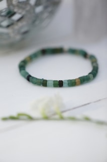 Stacked bracelets featuring tiny beads in ivory and sage tones, laid out on a subtle ivory background