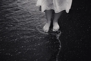 A cinematic portrait of a family walking barefoot along a shoreline, bathed in warm charcoal and sand tones.