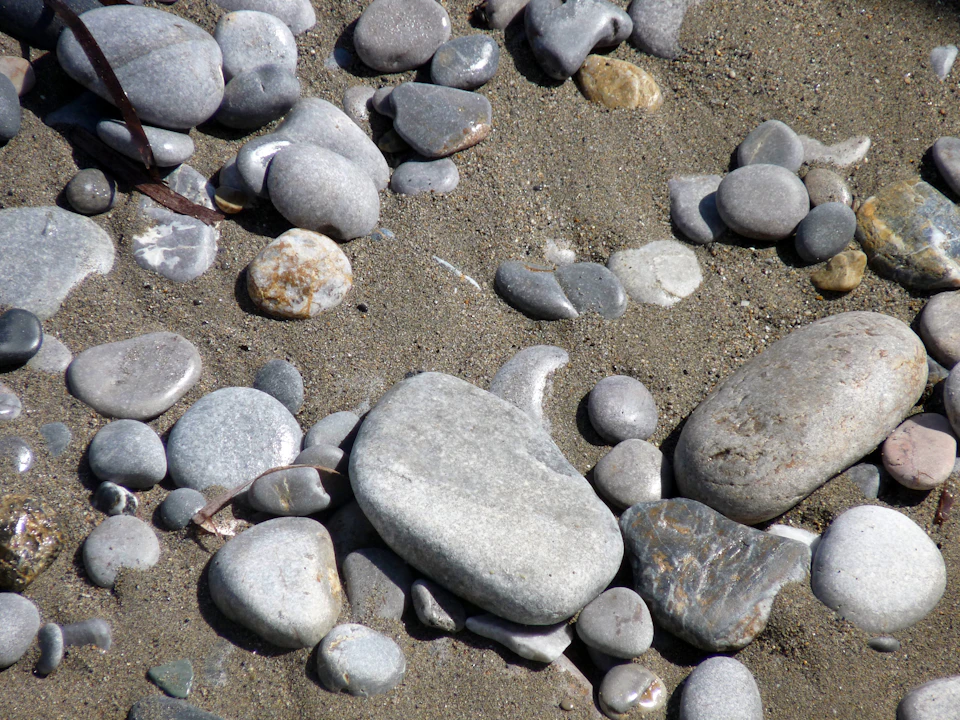 Close-up view of a rocky beach scene with diverse types of rocks scattered across sandy