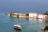 A serene coastal scene with a wooden boat sailing near a small island. The island features charming white Mediterranean-style buildings with tile roofs. Clear turquoise water surrounds the island, reflecting the vibrant colors of the landscape. Lush greenery is present on the island, enhancing the picturesque view.