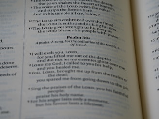 A close-up view of a page from a book, featuring text from biblical scripture. The focus is on Psalm 30, which is formatted with verse numbers and highlighted sections. The text appears printed in black on white paper, with a column layout and a slight shadow on the pages.