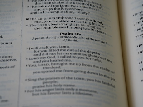 A close-up view of a page from a book, featuring text from biblical scripture. The focus is on Psalm 30, which is formatted with verse numbers and highlighted sections. The text appears printed in black on white paper, with a column layout and a slight shadow on the pages.