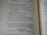 An open book with text visible on both pages. The blue and black text appears to include verses and religious references, indicating it might be a religious or spiritual text.