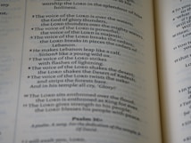 An open book with text visible on both pages. The blue and black text appears to include verses and religious references, indicating it might be a religious or spiritual text.