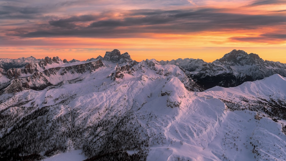 a mountain range covered in snow at sunset