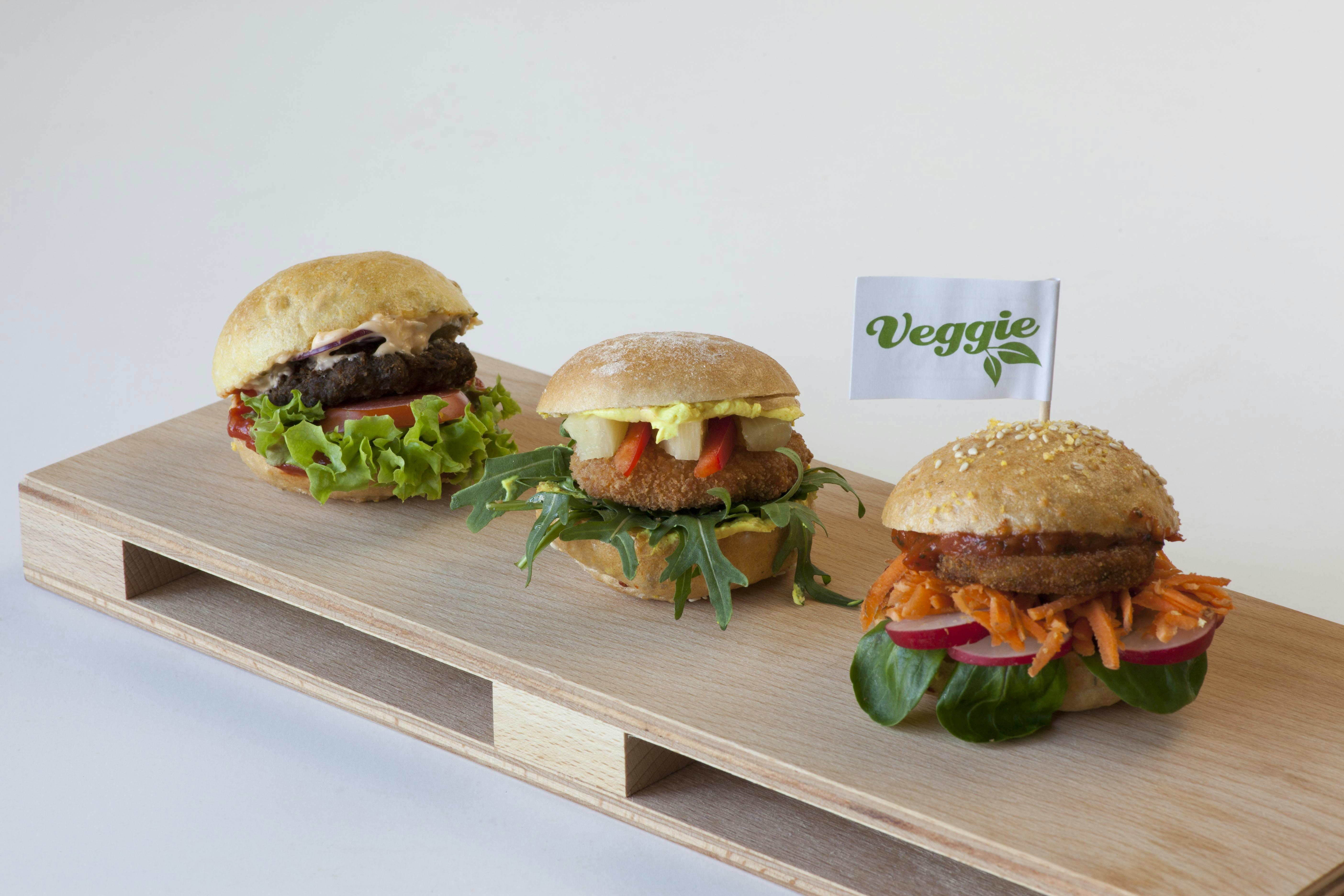 three burgers with lettuce, tomato, and other toppings on a