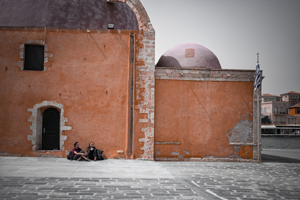 two people sitting on the ground in front of a building