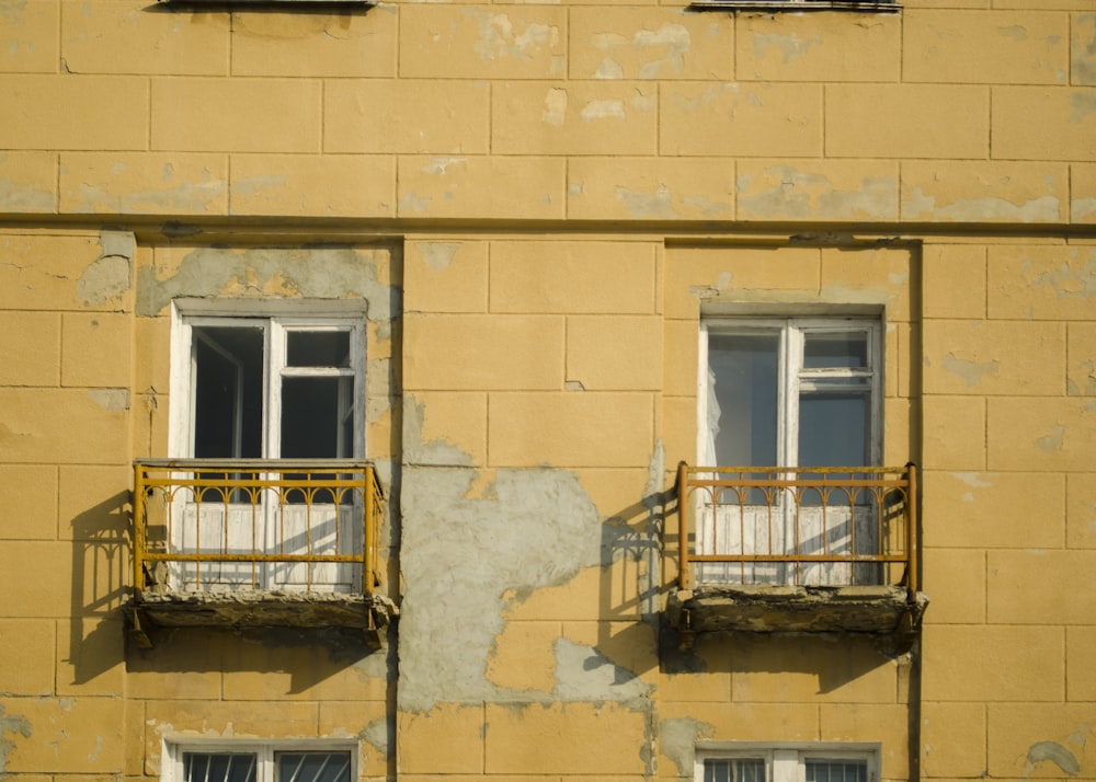 a yellow building with two balconies and two windows