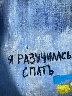 A textured blue canvas features Cyrillic text in bold black letters. In the lower right corner, there are abstract brushstrokes in bright blue and yellow.