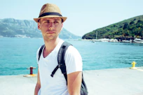 a man with a backpack and a hat standing in front of a body of water