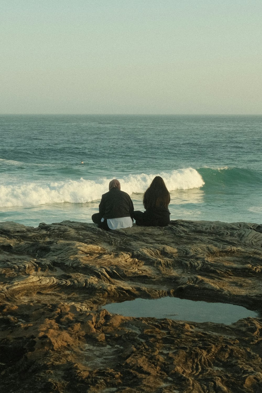 two people sitting on a rock looking out at the ocean