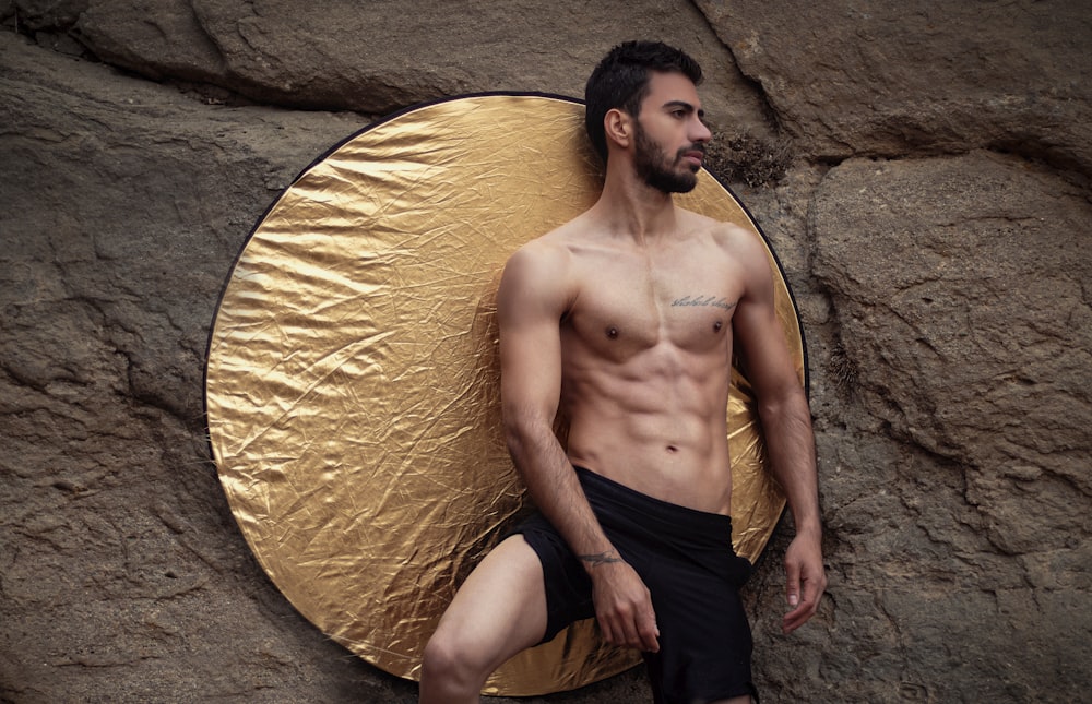 a shirtless man leaning against a rock