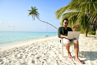 a man sitting in a chair on a beach using a laptop