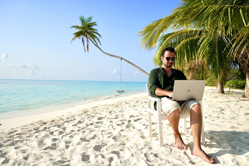a man sitting in a chair on a beach using a laptop