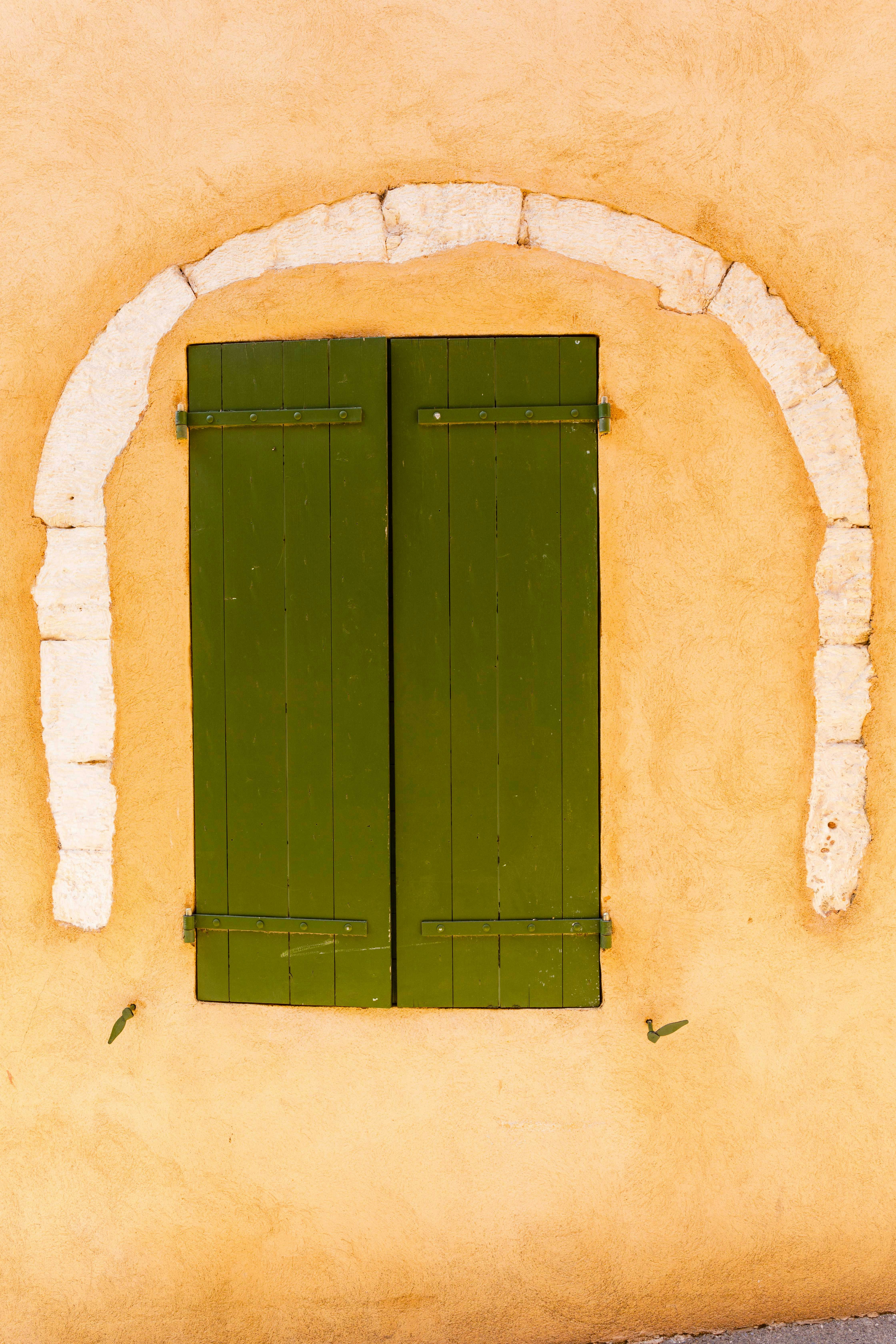 ein gelbes Gebäude mit grünen Fensterläden und einem weißen Bogen