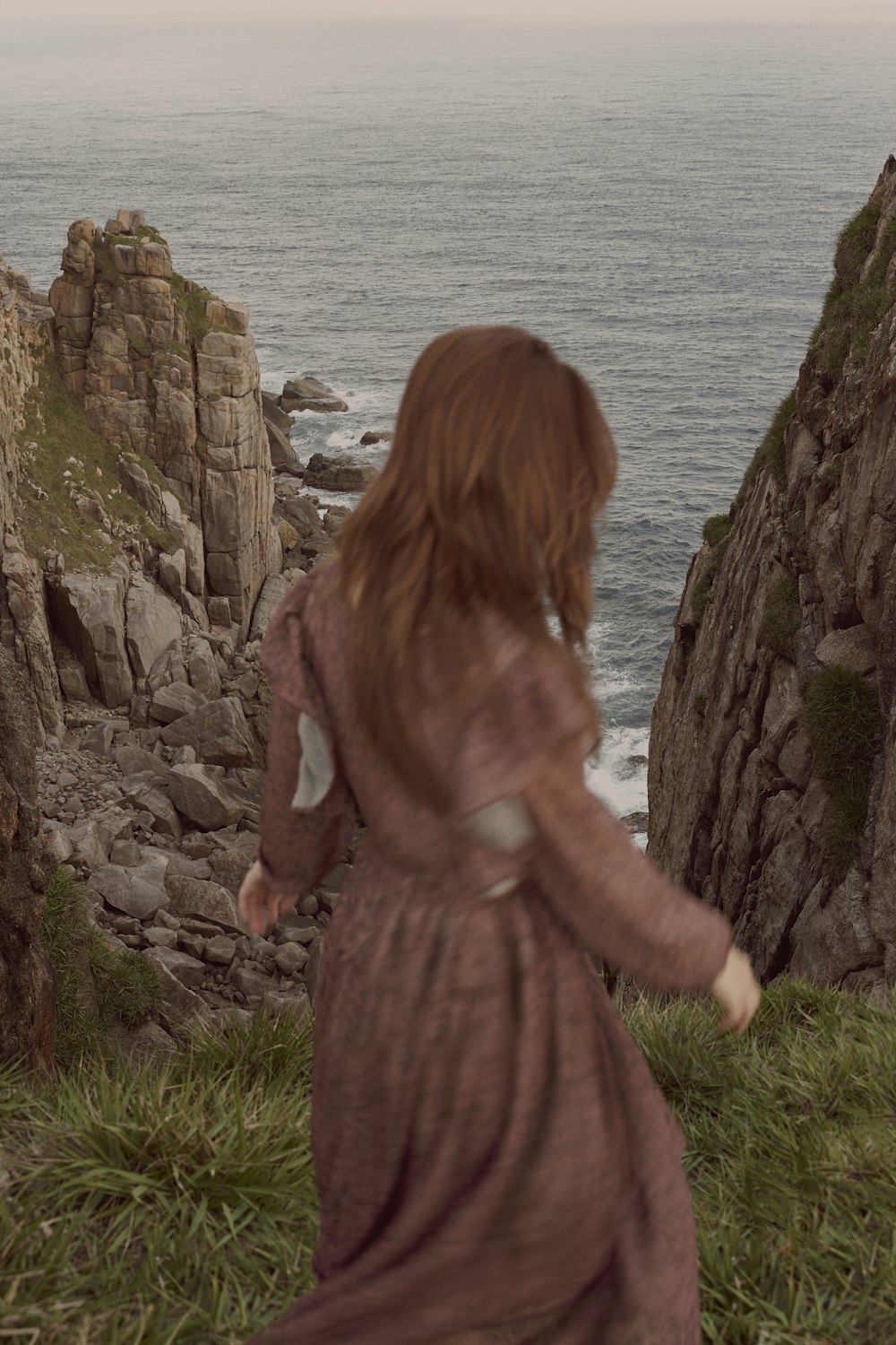 a woman in a long dress standing on a cliff by the ocean