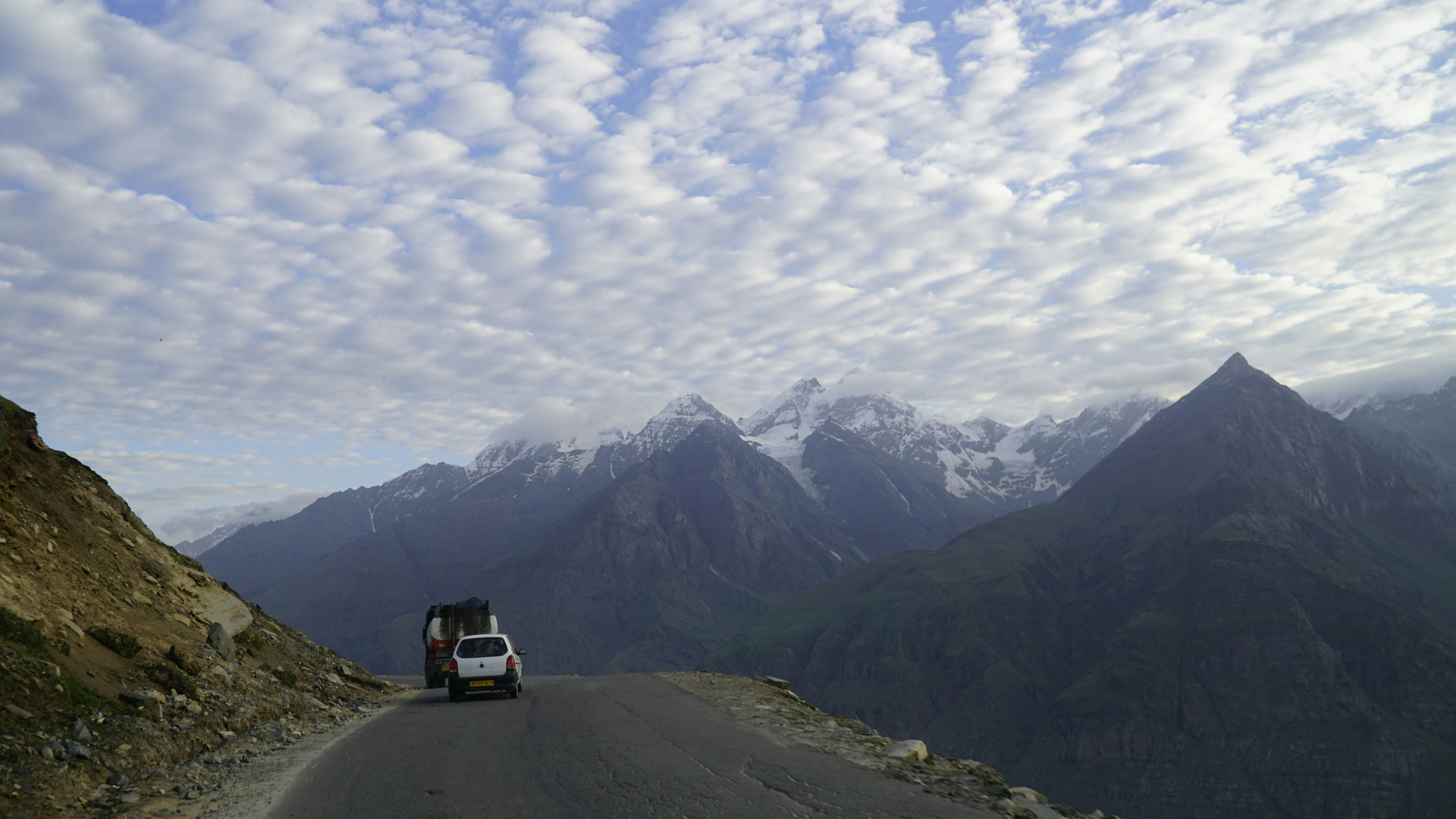 a truck driving down a road with mountains in the background