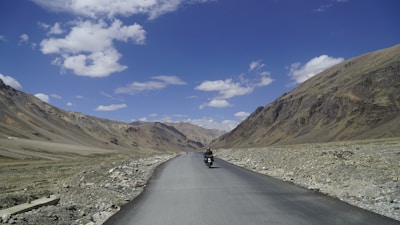 A biker riding along a scenic mountain road with clear blue skies overhead.