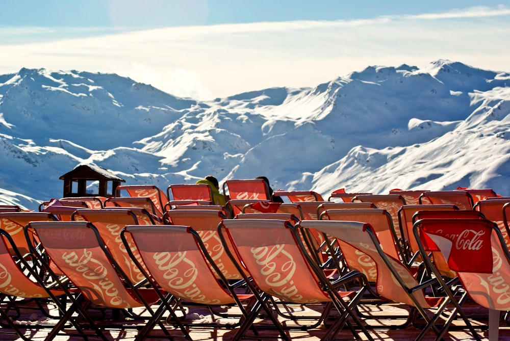 a row of chairs with coca - cola on them in front of a snowy mountain