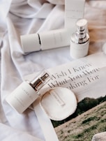A flat lay of skincare products, including bottles and a circular pad, placed on a silky fabric. There is also a magazine featuring an article with visible text 'Wish I Knew What You Were Looking For'. The overall aesthetic is minimalistic and elegant.