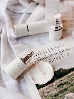 A flat lay of skincare products, including bottles and a circular pad, placed on a silky fabric. There is also a magazine featuring an article with visible text 'Wish I Knew What You Were Looking For'. The overall aesthetic is minimalistic and elegant.