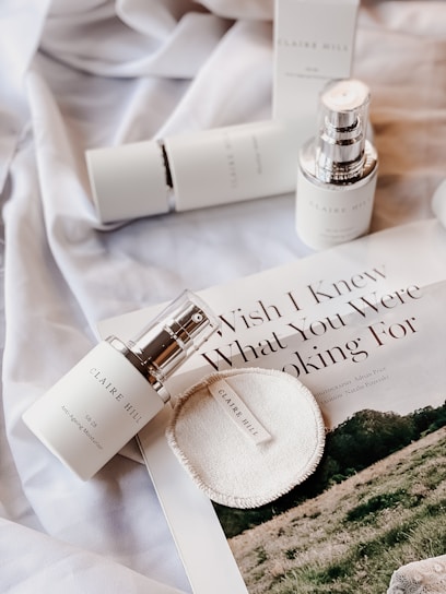A flat lay of skincare products, including bottles and a circular pad, placed on a silky fabric. There is also a magazine featuring an article with visible text 'Wish I Knew What You Were Looking For'. The overall aesthetic is minimalistic and elegant.