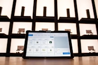 A tablet displaying a point-of-sale application sits on a countertop, with shelves in the background. The shelves are illuminated and contain cylindrical containers.