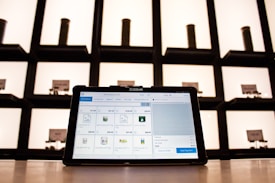A tablet displaying a point-of-sale application sits on a countertop, with shelves in the background. The shelves are illuminated and contain cylindrical containers.