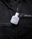 A white bottle labeled 'Sporty' eau de parfum is placed on a black jacket with quilted details. The name 'Alexander' is embroidered or printed on the jacket.