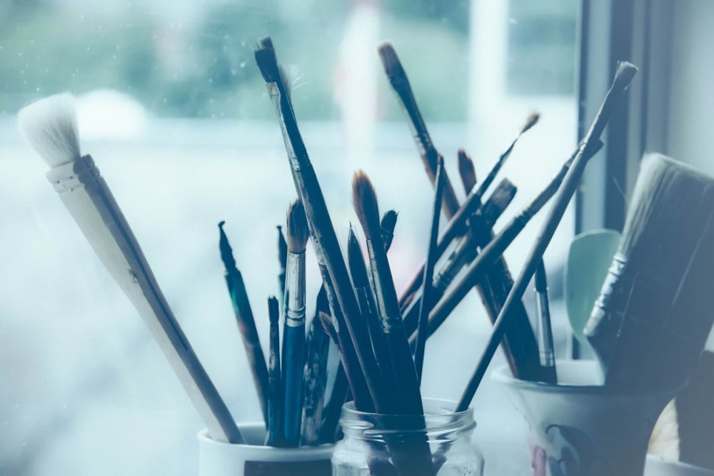 a glass jar filled with lots of paint brushes