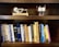 A wooden bookshelf holding a collection of books on various topics such as programming, dictionaries, and computer science. On the top shelf, there are two small mechanical models, one resembling a stirling engine and the other appearing to be a small engine with a propeller.