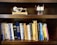 A wooden bookshelf holding a collection of books on various topics such as programming, dictionaries, and computer science. On the top shelf, there are two small mechanical models, one resembling a stirling engine and the other appearing to be a small engine with a propeller.