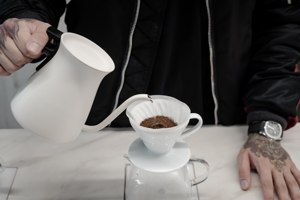 a person pouring coffee into a white pitcher