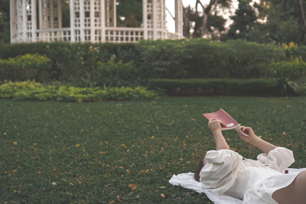 a woman laying in the grass reading a book