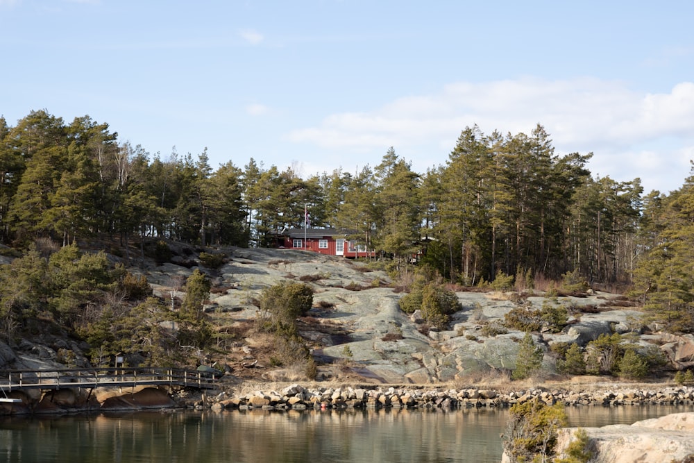 a red house on a rocky hill next to a body of water