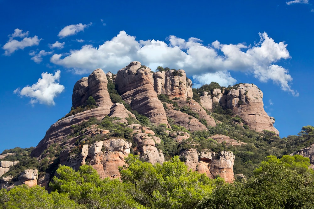 a rocky mountain with trees and clouds in the background